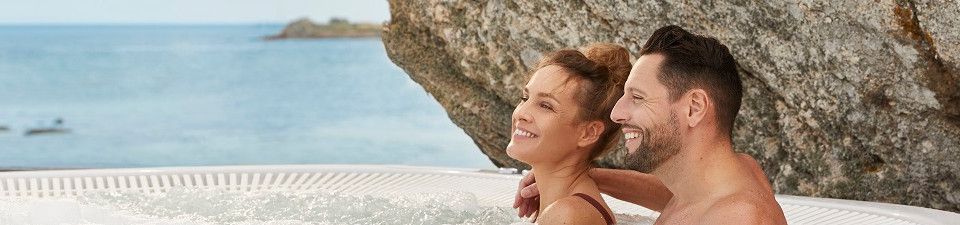 Couple profitant d’un bain à remous extérieur entouré de rochers face à la mer