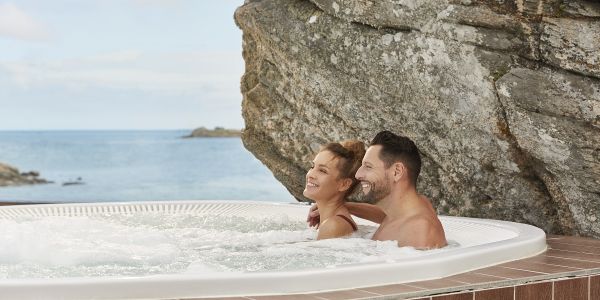 Couple profitant d’un bain à remous extérieur entouré de rochers face à la mer