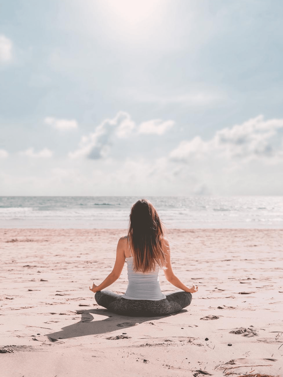 femme seule faisant du yoga sur la plage face à la mer