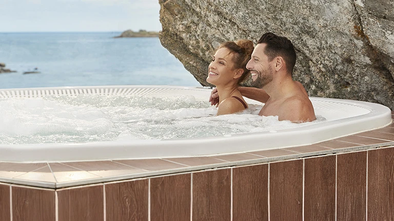 Couple profitant d’un bain à remous extérieur entouré de rochers face à la mer